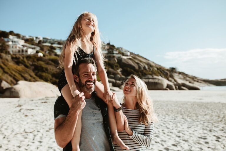 Family Beach Vacation in Perth: Father with daughter on shoulders, mother smiling. Deed of Family Arrangement with Clairs Keeley Lawyers.