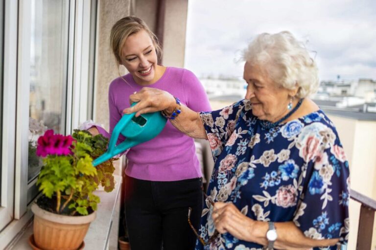 Enduring Power & Guardianship Perth: Woman helping elderly woman water plants on a balcony. Clairs Keeley Lawyers focus on elder care law.